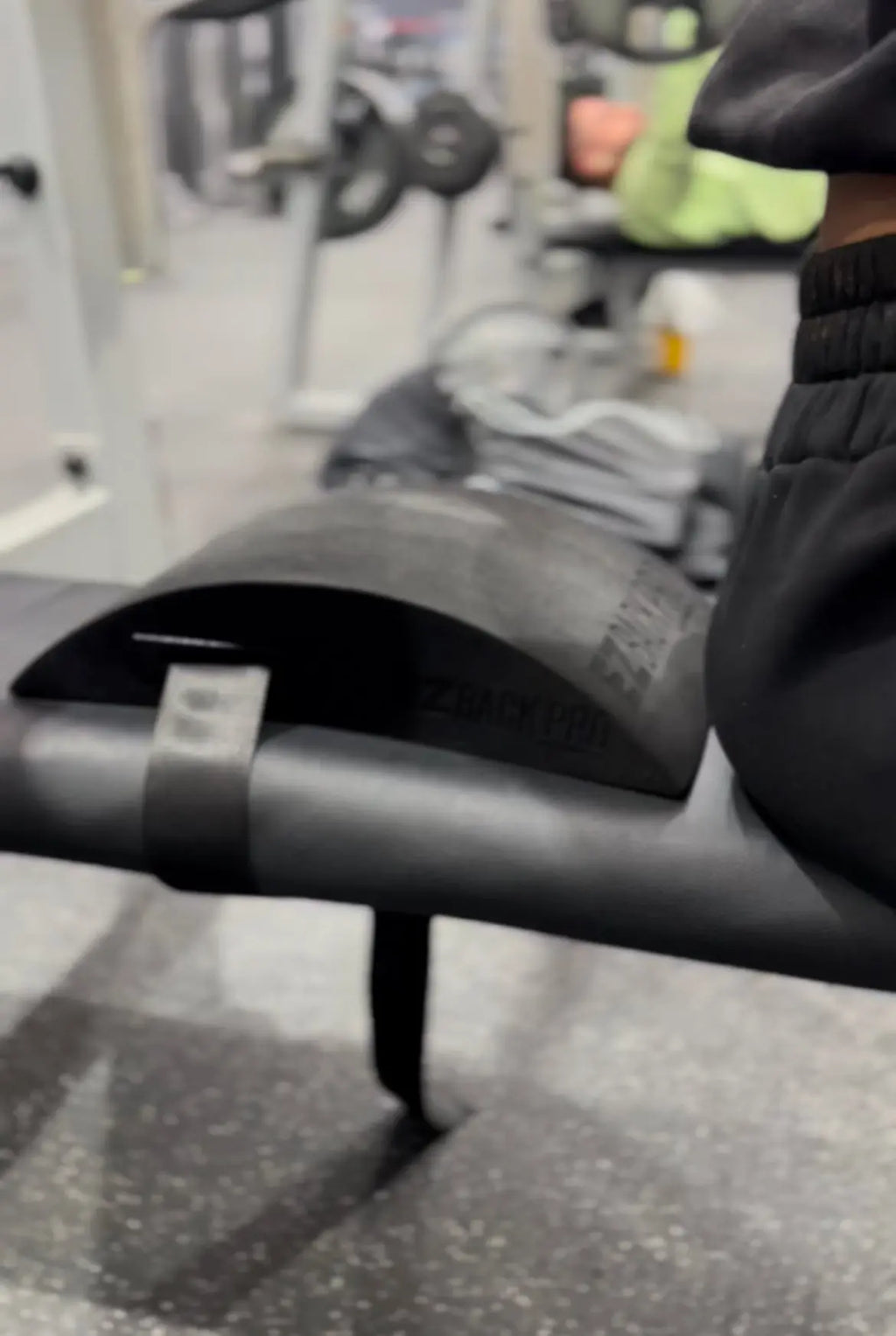Cherneka 'Sug Kneez' Johnson seated on a flat bench, preparing to lie back onto the EZBack Pro Level 2 strap for spinal alignment and posture support.