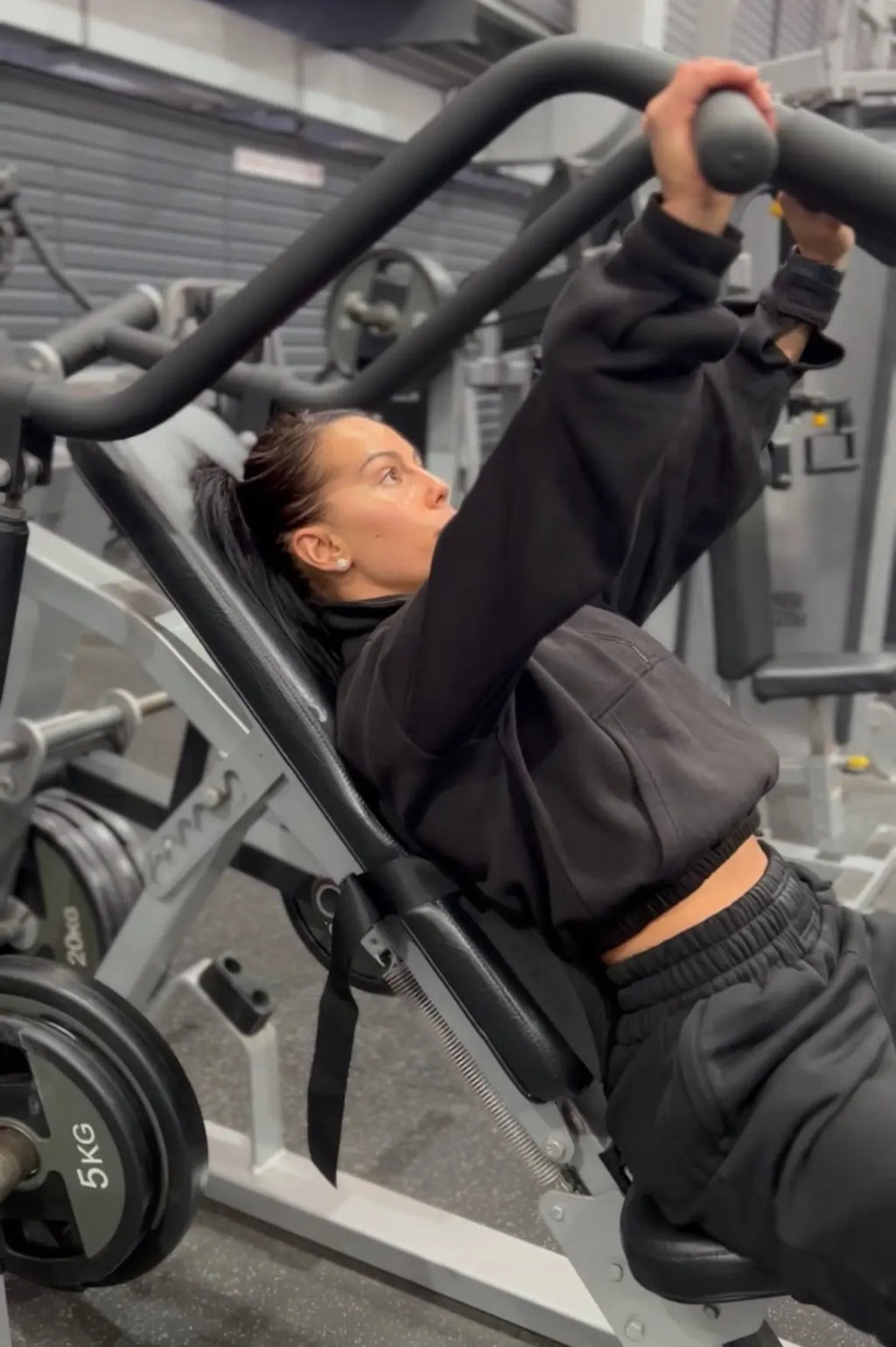 Cherneka 'Sug Kneez' Johnson using a Precor incline chest press machine with the EZBack Pro Level 2 strap positioned vertically for thoracic spine support.